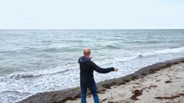 Sahilde suyun kenarında duran bir adam denize taş atıyor..