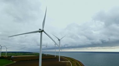 Bulutlu bir günde deniz kenarındaki modern beyaz rüzgar türbinleri temiz yeşil elektrik üretir..
