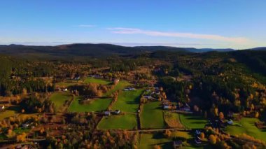 Güneş doğarken yeşil tarlaları, çiftlik evleri ve ormanları olan kırsal bir bölgede hava manzarası.