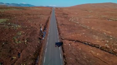 Dağlık arazide sonbahar renklerinde siyah bir araba sürüyordu. Hava takip kamerası, 4K video.