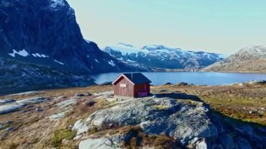 Yüksek dağlarda yüksek bir dağ yamacı olan küçük bir kulübe ve arka planda bir göl. 4K hava görüntüsü.
