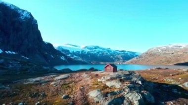 Yüksek dağlarda yüksek bir dağ yamacı olan küçük bir kulübe ve arka planda bir göl. 4K hava görüntüsü.