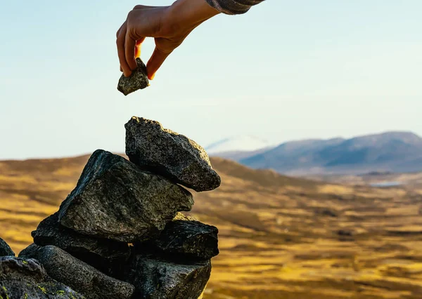 Hand placing a rock on top of a cairn on the peak of a mountain. Close up. . High quality photo
