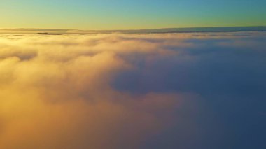 Turuncu güneş ışığı ve açık mavi gökyüzü ile beyaz bulutların üzerinde uçuyor..