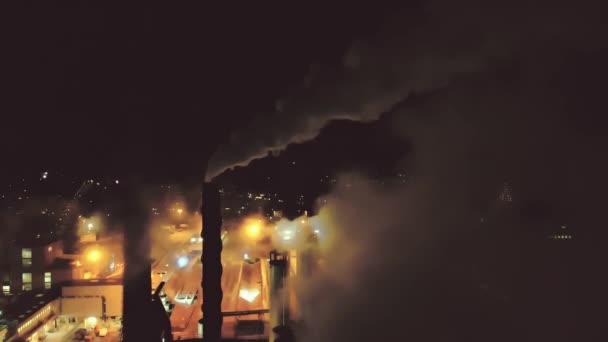 Velká továrna s hustým kouřem vycházejícím z komínů. Letecký noční záznam 4K.