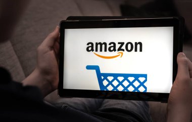 Siyah ekranda Amazon alışveriş logosu olan tableti tutan eller. Yüzeyin derinliği. Yüksek kalite fotoğraf