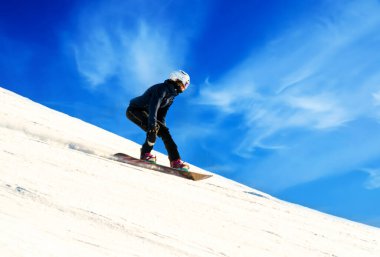 Güneşli bir günde açık mavi gökyüzüyle dik bir yamaçtan aşağı inen kadın snowboardcu. Yüksek kalite fotoğraf