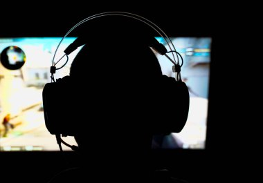 Karanlık bir odada, bir bilgisayarın üzerinde üç boyutlu nişancı oyunu oynayan birinin silueti. Yüzeyin derinliği. Yüksek kalite fotoğraf