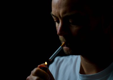 Az ışık alan bir ortamda sigara yakan bir adam. Siyah arkaplanda sığ bir alan derinliğinde izole edilmiş. Yüksek kalite fotoğraf