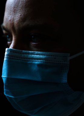 Yüz maskesi takan ve endişeli görünen beyaz bir adamın portresi. Siyah arkaplanda izole edilmiş sığ alan derinliği. Yüksek kalite fotoğraf