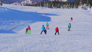 Kar kayakçıları ve snowboardcular, kış sporları tatil köyünde dik yamaçtan aşağı kayıyorlar..