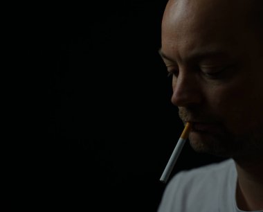 Ağzında sigarası yanmamış üzgün bir adamın portresi. Siyah arkaplanda sığ bir alan derinliğinde izole edilmiş. Yüksek kalite fotoğraf