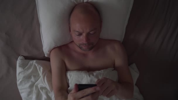 Seorang Pria Menggunakan Ponselnya Tempat Tidur Malam Hari Memeriksa Berita — Stok Video