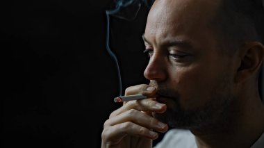 Sigara içen bir adama yaklaş. Siyah arkaplanda izole edilmiş, alan derinliği sığ. Yüksek kalite fotoğraf