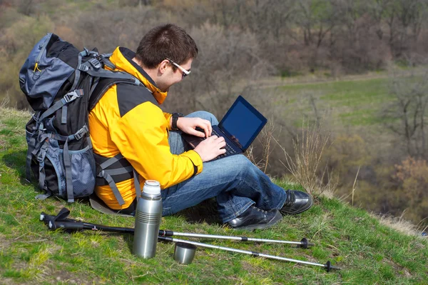 Turista com uma mochila e um laptop sentado na colina — Fotografia de Stock