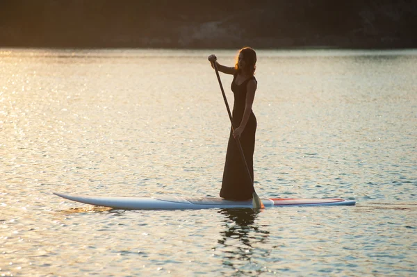 Chica delgada en stand up paddleboard sobre fondo de la puesta del sol. SUP02 — Foto de Stock