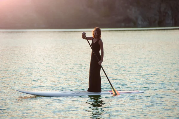 Chica delgada en stand up paddleboard sobre fondo de la puesta del sol. SUP01 — Foto de Stock