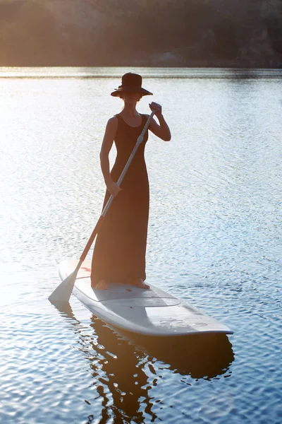 Smal flicka på stand up paddleboard på sunset bakgrund. Sup03 — Stockfoto