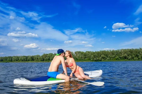 Giovane coppia seduta sul stand up paddle board bacio — Foto Stock