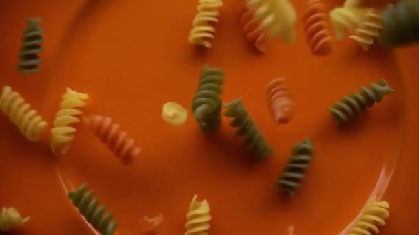 Rauwe veelkleurige macaroni pasta valt op de plaat, slow motion — Stockvideo