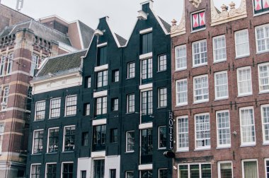 Hollanda, Amsterdam 'da klasik Hollandalı binalar ve otel, birçok açık pencereli kahverengi ve siyah tuğlalarla inşa ediliyor. Bulutlu bir gün.