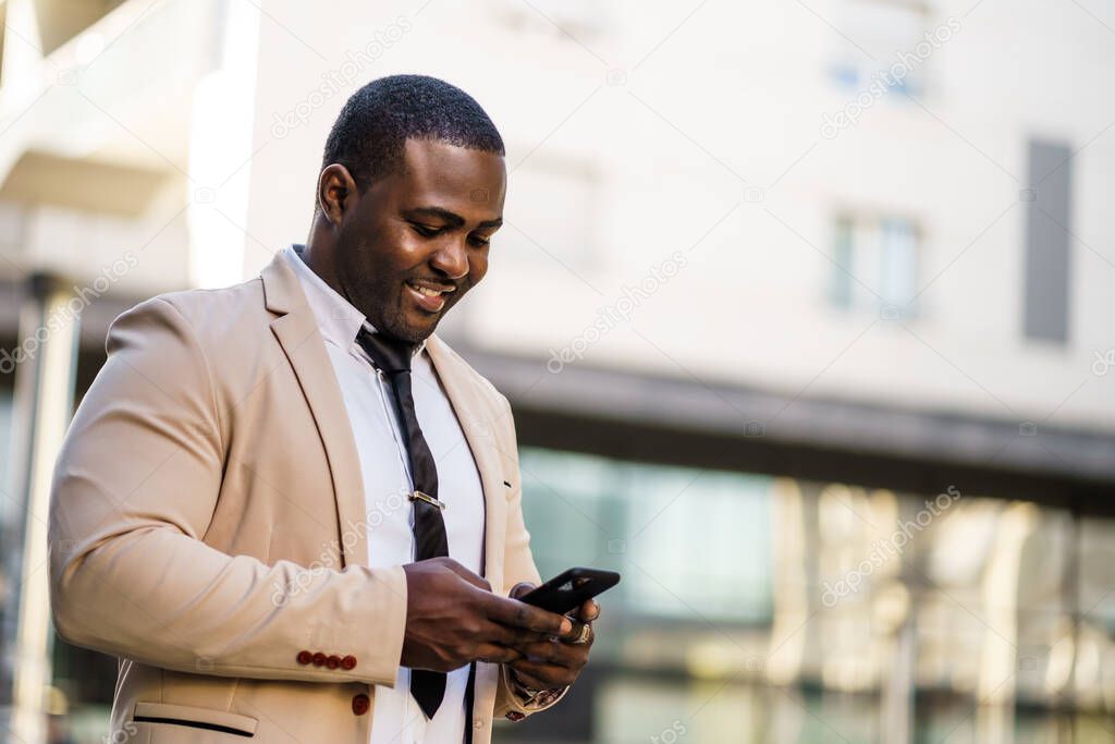 Portrait of happy african-american businessman who is using smartphone.