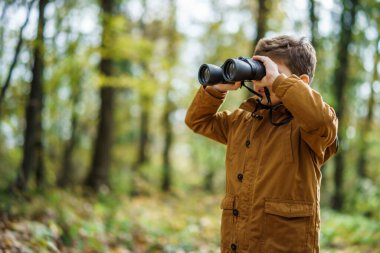 Boy is using binoculars in forest in autumn.