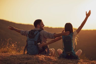 Genç mutlu çift dağda yürüyüş yapıyor ve gün batımını seyrediyor..