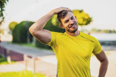 Genç adam dışarıda egzersiz yapıyor. Vücudunu esnetiyor ve koşuya hazırlanıyor..