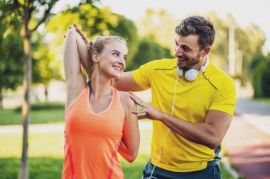 Genç çift dışarıda egzersiz yapıyor. Vücutlarını esnetiyorlar ve koşu için ısınıyorlar..