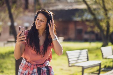 Mutlu genç bayan şehirde güneşli bir günün tadını çıkarıyor. Kulaklıkla müzik dinliyor..