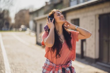 Mutlu genç bayan şehirde güneşli bir günün tadını çıkarıyor. Kulaklıkla müzik dinliyor..