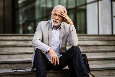 Kıdemli işadamı çalışmaktan yoruldu. Şirket binasının önünde oturuyor ve başı ağrıyor..
