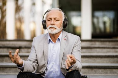 Mutlu kıdemli işadamı şirket binasının önünde meditasyon yapıyor..