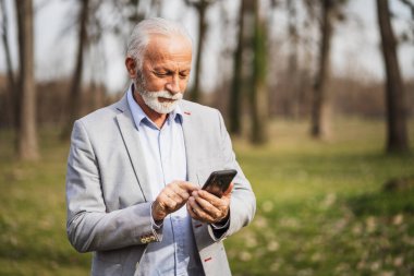 Mutlu kıdemli işadamı işten sonra dinleniyor. Akıllı telefondan mesajlaşıyor..