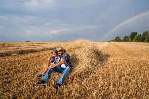 収穫が成功した後 父と息子は休んでいます 後ろの空の虹 — ストック写真