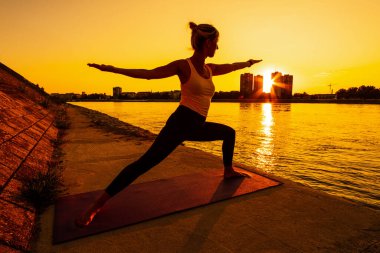 Genç bayan dışarıda egzersiz yapıyor. Güneşli bir günde yoga yapıyor. Virabhadrasana / Savaşçı 2 poz.