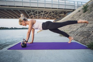 Kettlebell pilatesini dışarıda yapan bir kadın. Kalas, bacak kaldırma egzersizi..