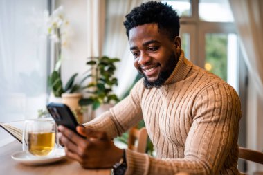 Barda sıradan giyinmiş mutlu bir zenci portresi. Çevrimiçi akıllı telefon ve mesajlaşma kullanıyor..