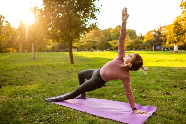 Sonbaharda parkta pilates yapan yetişkin bir kadın. Sağlıklı bir yaşam tarzı. Yan kalas egzersizi..