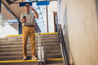 Kıdemli adam tren istasyonunda duruyor ve akıllı telefondan mesaj yolluyor. Perişan halde. Son sınıflar seyahat ediyor..