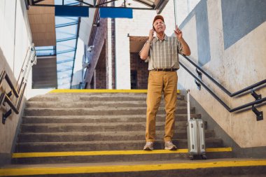 Kıdemli adam tren istasyonunda duruyor ve cep telefonuyla konuşuyor. Perişan halde. Son sınıflar seyahat ediyor..