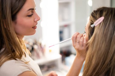 Makyaj sanatçısı bir müşteri oturumu yapıyor, muhtemelen bir gelin ya da olay görüntüsü için, kozmetik uygulamasında detaylara ve becerilere dikkat çekiyor.