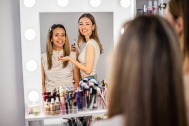 İşteki güzellik uzmanı. Genç kadın güzellik stüdyosunda makyöz olarak çalışıyor. Göz farı sürüyor. Her iki kadın da tarafsız bluz ve kot pantolon giyiyor..