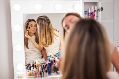 Güzellik uzmanı müşterinin yüzü üzerinde dikkatle çalışıyor. Yüz pudrası sürüyor ve allık sürerek yumuşatıyor..