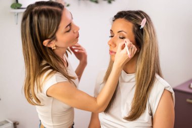 Güzellik uzmanı müşterinin yüzü üzerinde dikkatle çalışıyor. Müşteri sakince oturup makyaj seansının tadını çıkarırken o göz kalemi sürüyor..