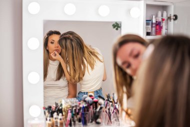 İşteki güzellik uzmanı. Genç kadın güzellik stüdyosunda makyöz olarak çalışıyor. Bir müşterisine ruj sürüyor..