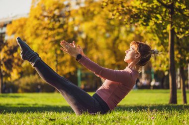 Sonbaharda parkta pilates yapan yetişkin bir kadın. Sağlıklı bir yaşam tarzı. Teaser egzersizi.