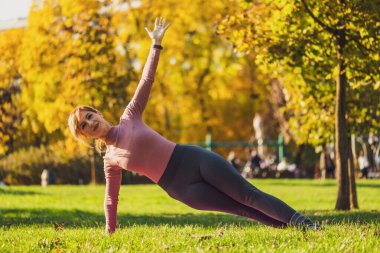 Sonbaharda parkta pilates yapan yetişkin bir kadın. Sağlıklı bir yaşam tarzı. Yan kalas egzersizi..