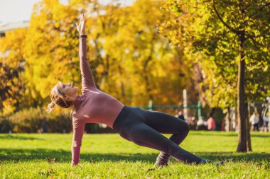 Sonbaharda parkta pilates yapan yetişkin bir kadın. Sağlıklı bir yaşam tarzı. Yan kalas egzersizi..